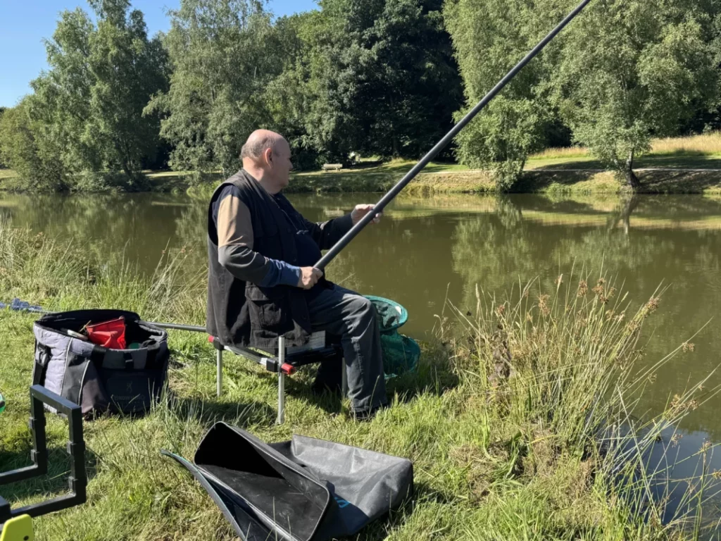 Un pêcheur vient de mettre sa canne à l'eau. Il est assis et attend.