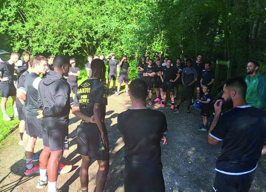 Les joueurs sont en rond avec le coach. Ils sont sous des arbres.