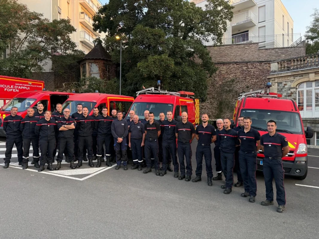 Les pompiers sont réunis en groupe devant des véhicules.