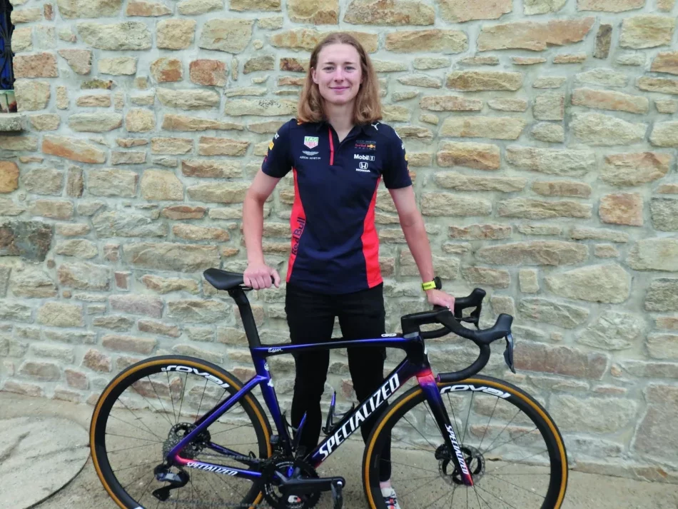 Une fille est debout derrière son vélo. Elle est en tenue de cycliste.