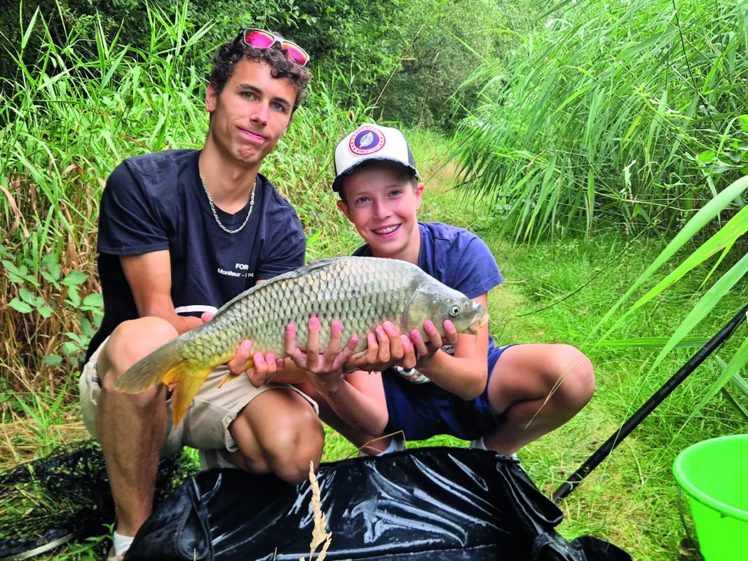 L'animateur tient une carpe avec un enfant.