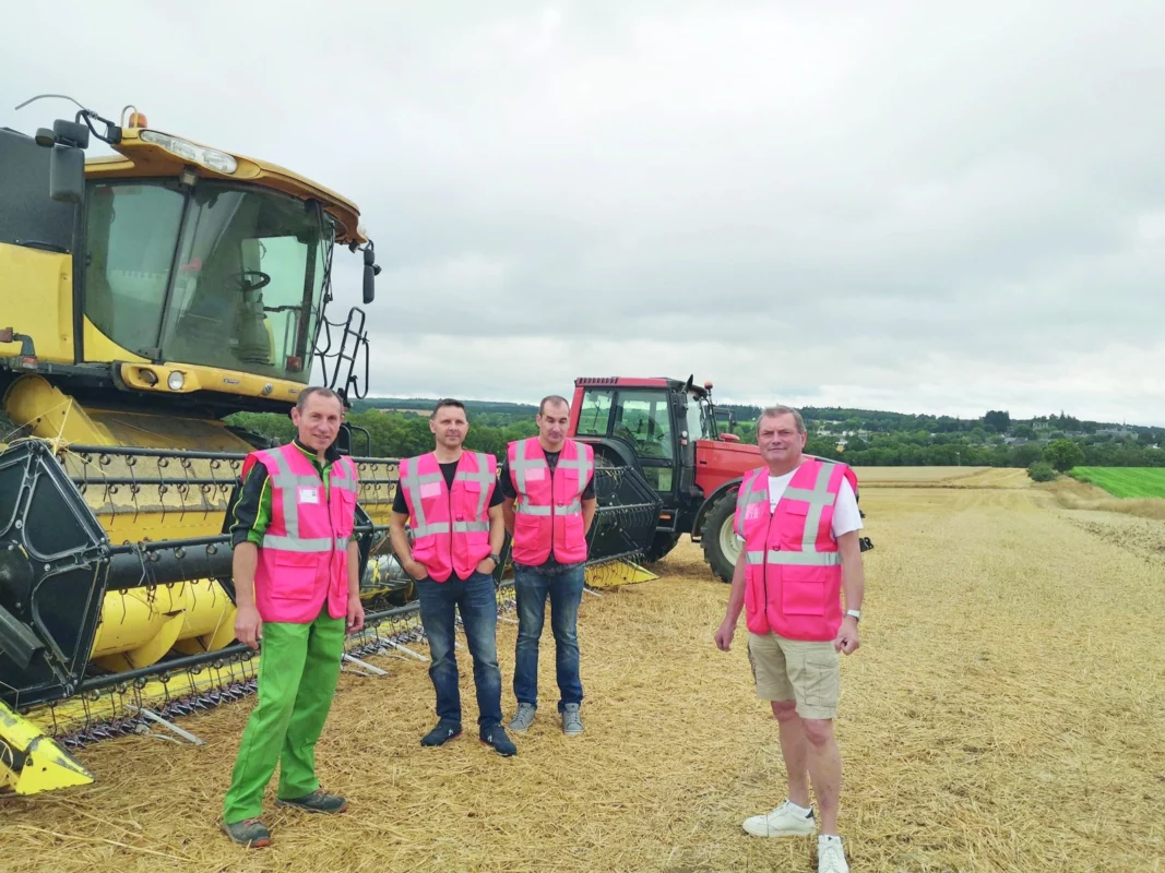 Quatre personnes avec des gilets rouges se tiennent debout devant une moissonneuse et un tracteur.